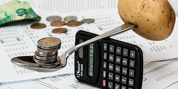 Geld und Kartoffel balancieren auf Taschenrechner, darunter Rechnungen