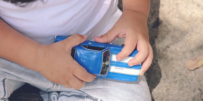Kind hält blaues Spielzeugauto in der Hand